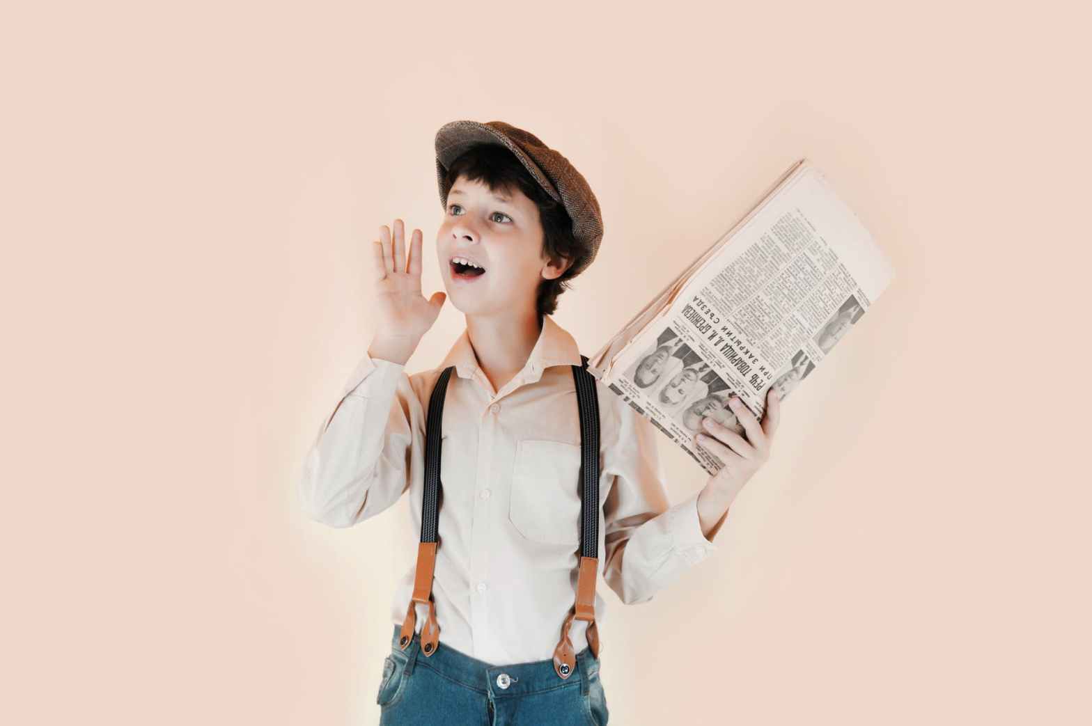 cheerful boy holding aged newspaper against beige background