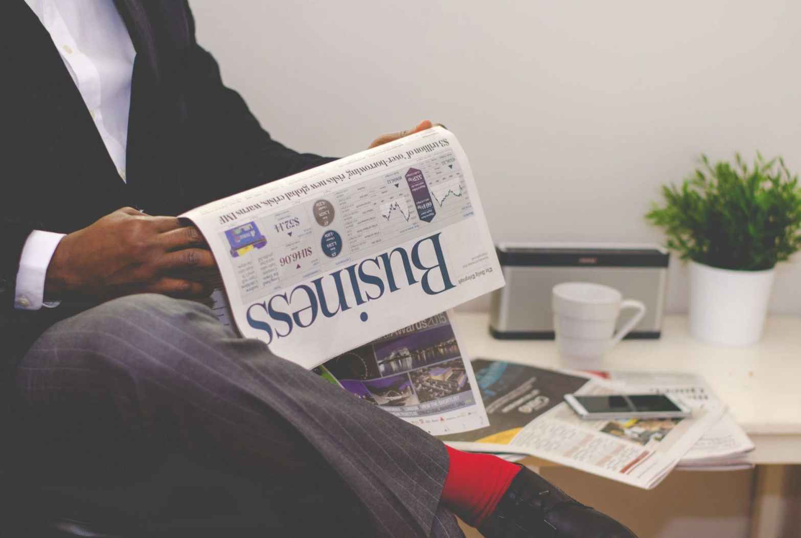 man reading newspaper while sitting near table with smartphone and cup for an article about how to write the perfect pitch with examples for the best media relations and earned media coverage